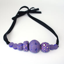 Load image into Gallery viewer, Measurements: each bead is between 1.5cm to 3.5cm Each design is exclusively unique and one of a kind! Finished with a lovely black ribbon tie so you can adjust the necklace length. A beautiful, bold and colourful statement necklace featuring eight different millefiori style handmade beads. The colours are purple, pink and white.