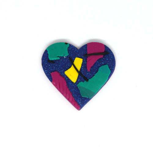 A wonderful statement piece of wearable art! A unique heart shaped brooch that has an abstract 80's vibe! Vibrant green, yellow and pink overlay a glittery blue base! Detailed with texture and strands of black clay!
