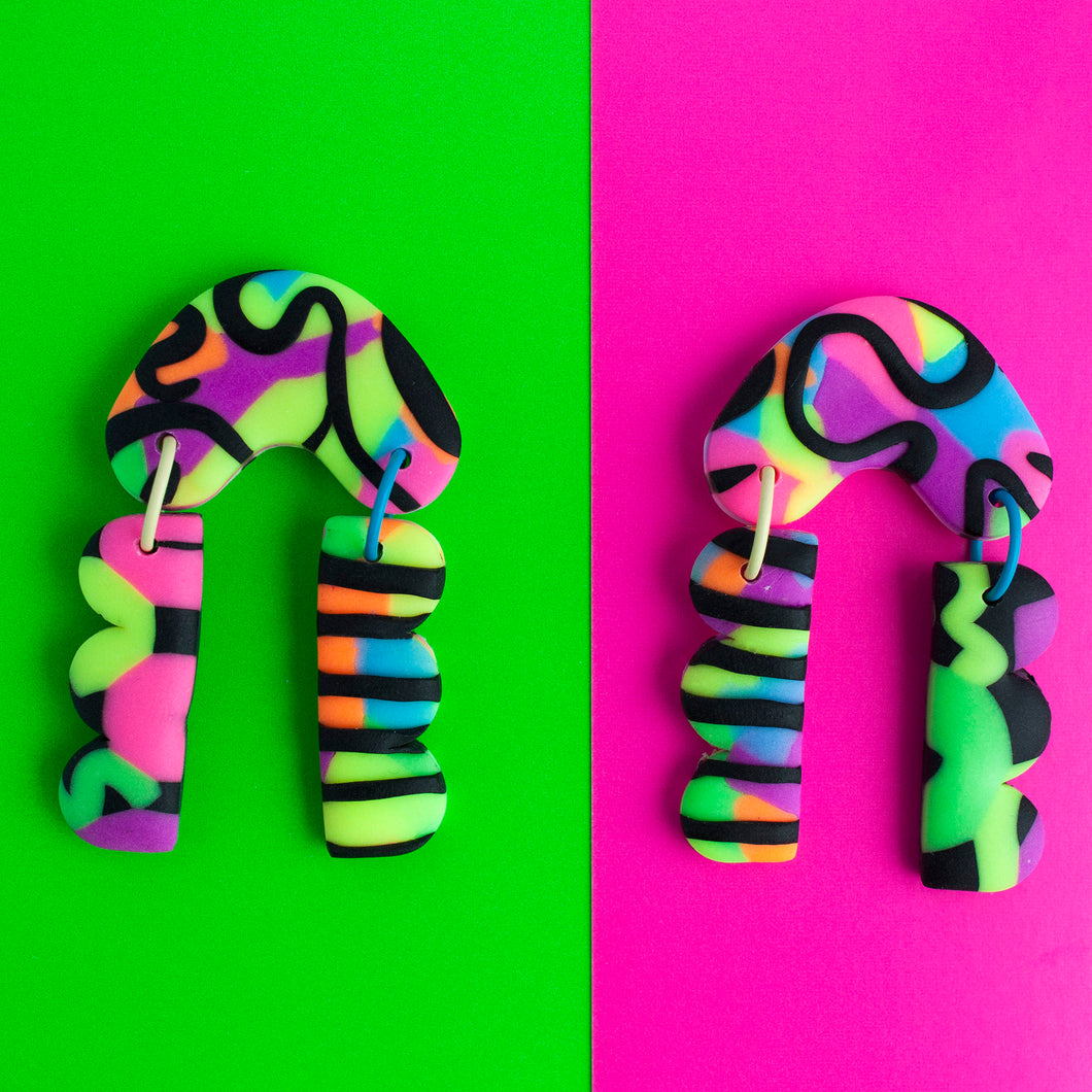 Status Collection throwback to the 80's legwarmers trend! These vibrant dangle earrings have bold and colourful multi coloured neon accentuated with black swirls and stripes! Completed with yellow and blue jump rings!
