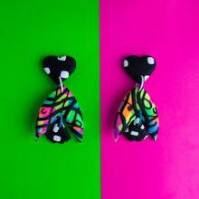 Load image into Gallery viewer, A standout statement from the Status Collection! These bright earrings have three pieces that swing beautifully! A black heart top with white dashes. In the middle, a unique batwing shaped multi coloured neon base with black swirls. Lastly, a black and white mini moth wing at the bottom to match the top pattern!