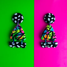 Load image into Gallery viewer, Gorgeous earrings from the Status Collection! These bright earrings have three pieces that swing beautifully! A black circle top with white dashes. In the middle, a moth wing shaped multi coloured neon base with black swirls. Lastly, a black and white triple bump! Lilac, purple and blue jump rings connect all the pieces together!
