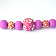 Load image into Gallery viewer, A bold and colourful statement necklace featuring millefiori style handmade beads. Seven beautiful beads decorated with purples, pinks, white and mustard yellow. With a black ribbon tie closure