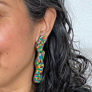 Model wears mosaic rocks squiggle earrings with a beautiful pattern of marbled brown, green, cream, bright red, electric blue, mango orange with a chocolate coloured brown base. 
