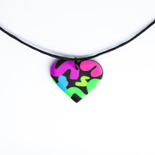 Load image into Gallery viewer, The Status Heart Pendant Necklace has squiggles of neon purple, neon pink, neon blue, neon yellow and neon green against a black background. With a waxed black cotton cord.