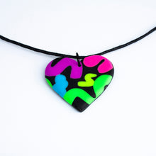 Load image into Gallery viewer, The heart pendant has squiggles of neon purple, neon pink, neon blue, neon yellow and neon green against a black background. With a waxed black cotton cord.