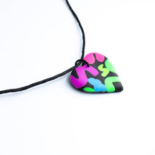 Load image into Gallery viewer, Side view of a heart pendant which has squiggles of neon purple, neon pink, neon blue, neon yellow and neon green against a black background. With a waxed black cotton cord.