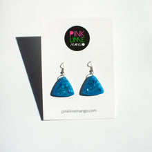 Load image into Gallery viewer, glittery blue resin triangle earrings with silver plated hooks placed on a Pink Lime Mango backing card.