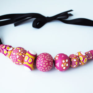 Measurements: each bead is between 1.5cm to 3cm Each design is exclusively unique and one of a kind! Finished with a lovely black ribbon tie so you can adjust the necklace length. A bold and colourful statement necklace featuring eleven different millefiori style handmade beads. The colours are purple, pink, white and mustard yellow.