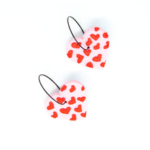 Load image into Gallery viewer, Gratitude Hoops - handcrafted light pink hearts with a small red hearts texture laid across the surface. Attached with black hypoallergenic stainless steel hoops.