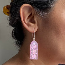 Load image into Gallery viewer, Delicate arches of clear resin with bursts of pale pink and tiny shimmery flower sequins. The unique V shaped earring hooks are made of sterling silver. Model shot

