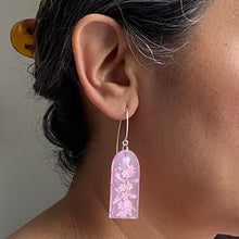 Load image into Gallery viewer, Delicate arches of clear resin with bursts of pale pink and tiny shimmery flower sequins. The unique V shaped earring hooks are made of sterling silver. Model shot
