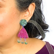 Load image into Gallery viewer, Model shot. Handcrafted resin earrings decorated with teal blue and purple glitter. The round stud top has a been jam packed with gorgeous sparkly blue and green glitter. The middle triangle piece is fabulously purple and glittery! The three bumps piece at the bottom has clear resin with teal glitter edging.