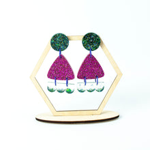 Load image into Gallery viewer, Earrings displayed on a hexagonal display stand. Handcrafted resin earrings decorated with teal blue and purple glitter. The round stud top has a been jam packed with gorgeous sparkly blue and green glitter. The middle triangle piece is fabulously purple and glittery! The three bumps piece at the bottom has clear resin with teal glitter edging.