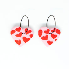 Load image into Gallery viewer, Bright, bold, and colourful with hypoallergenic black hoops. The earrings have been finished with a silky smooth back so they feel luxurious to touch. A beautiful contrast to the raised texture at the front. Each individual red heart has been cut by hand by Vicky, artist and founder of Pink Lime Mango. The heart earrings have a light pink base and are made from lightweight polymer clay.