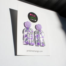 Load image into Gallery viewer, Gorgeous handcrafted resin earrings with round glittery lilac stud tops! These beautiful arch dangle earrings are decorated with delicate pieces of silver and purple foils. Pictured with a Pink Lime Mango earring backing card. Side view.