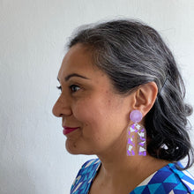 Load image into Gallery viewer, Gorgeous handcrafted resin earrings with round glittery lilac stud tops! These beautiful arch dangle earrings are decorated with delicate pieces of silver and purple foils. Model side view.
