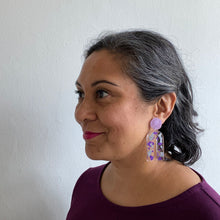 Load image into Gallery viewer, Gorgeous handcrafted resin earrings with round glittery lilac stud tops! These beautiful arch dangle earrings are decorated with delicate pieces of silver and purple foils. Model shot.