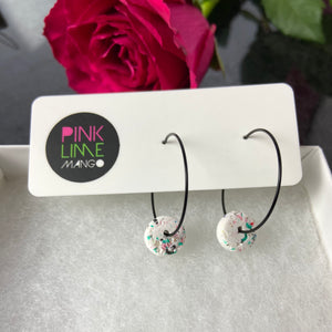 Black hoops with white polymer clay circles on an earring card on a box with a rose behind