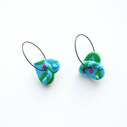 A unique, joyful and vibrant earring design! The caterpillar makes the little heart hang upside! Hence the name wonky heart caterpillar hoops!  Abstract blue, green and pink detailing on a light blue small heart shaped base. Styled with contemporary stainless steel black hoops. Lightweight, handcrafted and one of a kind!
