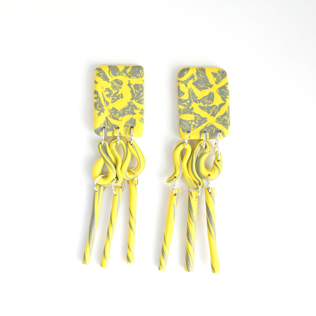 These are the beautiful Hope Dangles. The top rectangular pieces have a unique yellow and grey pattern with a silver plated stud top fixing at the back. The middle section swirls with both colours and then is completed with a delicate triple tube fringe. 