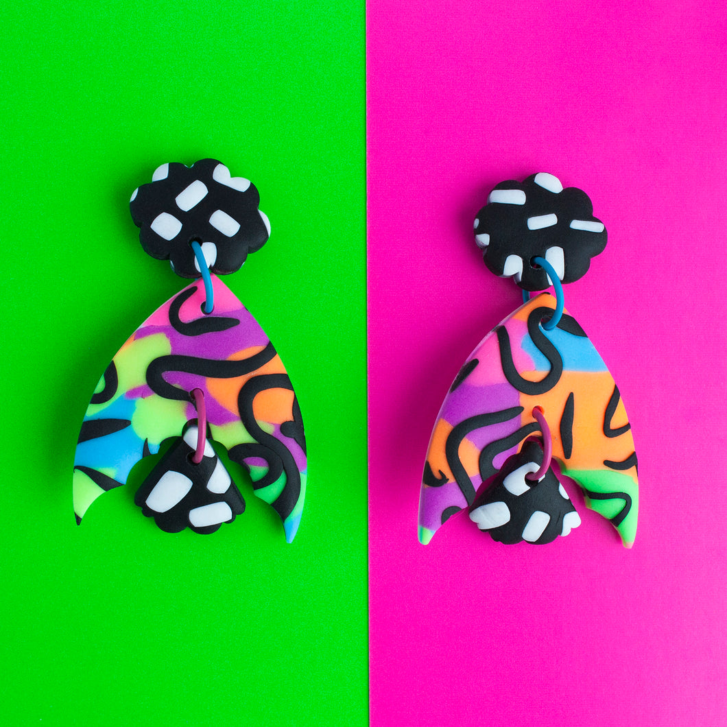 A standout statement from the Status Collection! These bright earrings have three pieces that swing beautifully! A black flower top with white dashes. In the middle, a unique batwing shaped multi coloured neon base with black swirls. Lastly, a black and white mini moth wing at the bottom to match the top pattern!