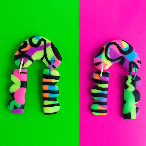 Status Collection throwback to the 80's legwarmers trend! These vibrant dangle earrings have bold and colourful multi coloured neon accentuated with black swirls and stripes! Completed with yellow and blue jump rings!