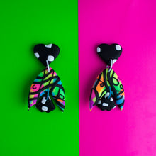 Load image into Gallery viewer, A standout statement from the Status Collection! These bright earrings have three pieces that swing beautifully! A black heart top with white dashes. In the middle, a unique batwing shaped multi coloured neon base with black swirls. Lastly, a black and white mini moth wing at the bottom to match the top pattern!
