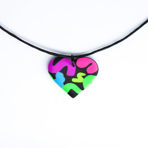 The Status Heart Pendant Necklace has squiggles of neon purple, neon pink, neon blue, neon yellow and neon green against a black background. With a waxed black cotton cord.