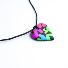 Load image into Gallery viewer, Side view of a heart pendant which has squiggles of neon purple, neon pink, neon blue, neon yellow and neon green against a black background. With a waxed black cotton cord.
