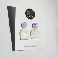 Load image into Gallery viewer, Arch shaped colour shift dangle earrings with lilac glitter stud tops. Photographed on a Pink Lime Mango backing card
