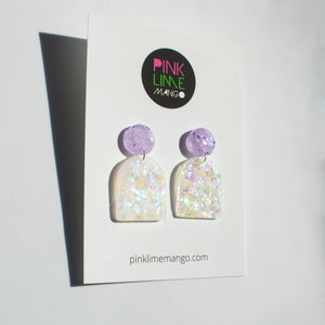 Arch shaped colour shift dangle earrings with lilac glitter stud tops. Photographed on a Pink Lime Mango backing card