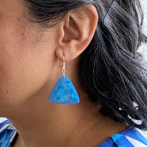 glittery blue resin triangle earrings with silver plated hooks. model shot.