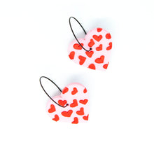 Load image into Gallery viewer, Gratitude Hoops - handcrafted light pink hearts with a small red hearts texture laid across the surface. Attached with black hypoallergenic stainless steel hoops.
