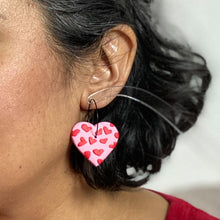 Load image into Gallery viewer, Model Shot - Gratitude Hoops - handcrafted light pink hearts with a small red hearts texture laid across the surface. Attached with black hypoallergenic stainless steel hoops.

