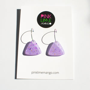Sparkly lilac triangular earrings from the Under the Sea resin collection. Beautiful layers of fine iridescent glitter, colour shifting aurora flakes and tiny pieces of metallic purple foil. A unique design that has been complimented with multicoloured rainbow hoops! With a Pink Lime Mango backing card.