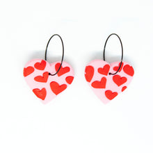 Load image into Gallery viewer, Bright, bold, and colourful with hypoallergenic black hoops. The earrings have been finished with a silky smooth back so they feel luxurious to touch. A beautiful contrast to the raised texture at the front. Each individual red heart has been cut by hand by Vicky, artist and founder of Pink Lime Mango. The heart earrings have a light pink base and are made from lightweight polymer clay.
