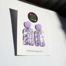 Load image into Gallery viewer, Gorgeous handcrafted resin earrings with round glittery lilac stud tops! These beautiful arch dangle earrings are decorated with delicate pieces of silver and purple foils. Pictured with a Pink Lime Mango earring backing card. Side view.
